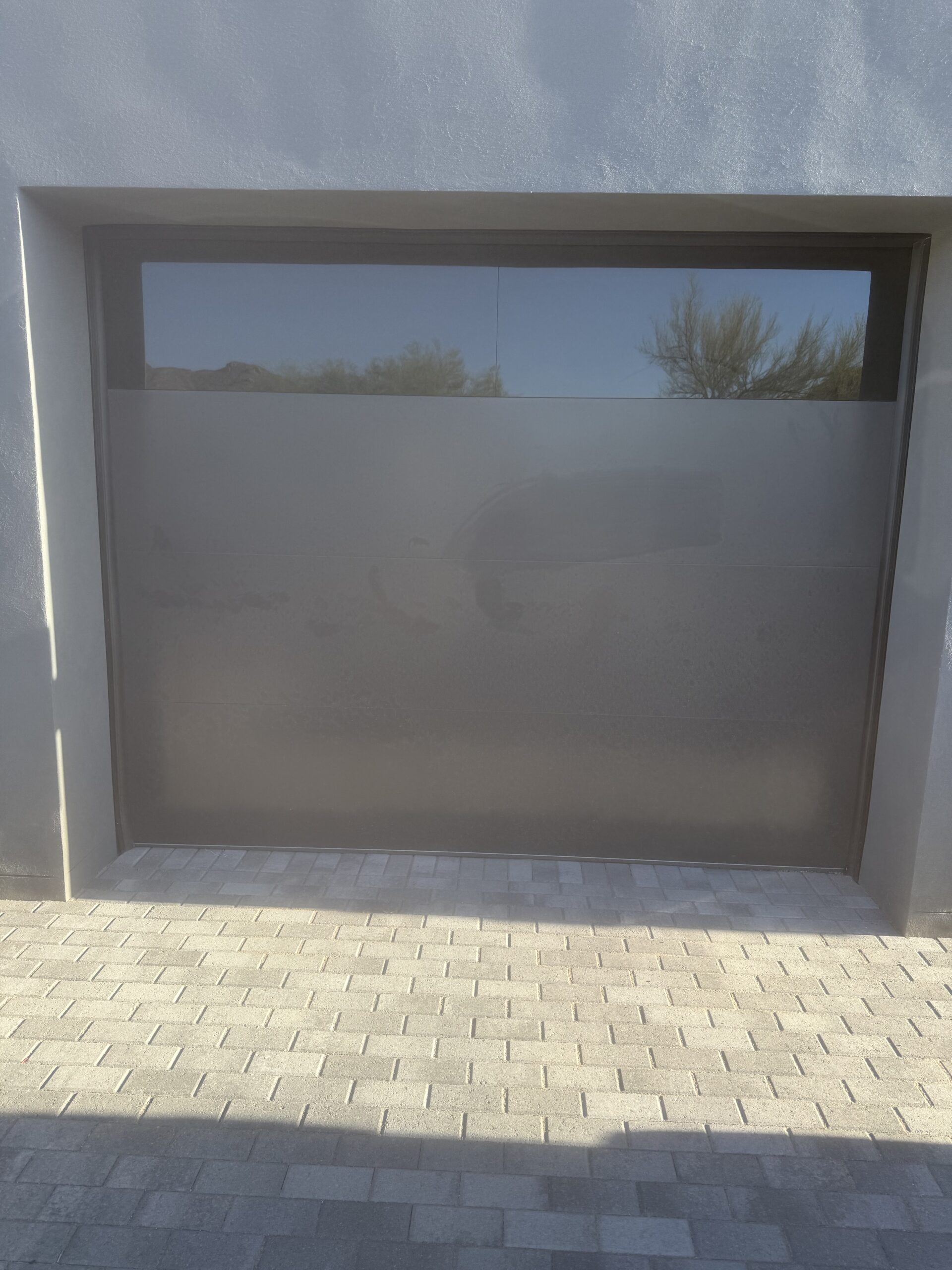 Modern garage door installation with sleek design, reflecting surroundings, and paver driveway, showcasing AZ Garage Door Pros LLC's quality workmanship.