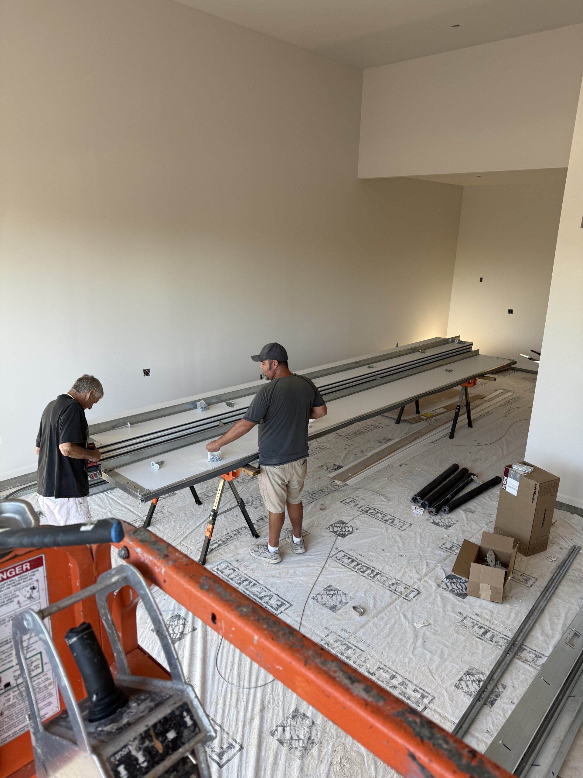 Two technicians assembling garage door components in a spacious interior, with tools and materials on the floor, showcasing AZ Garage Door Pros LLC's installation services.