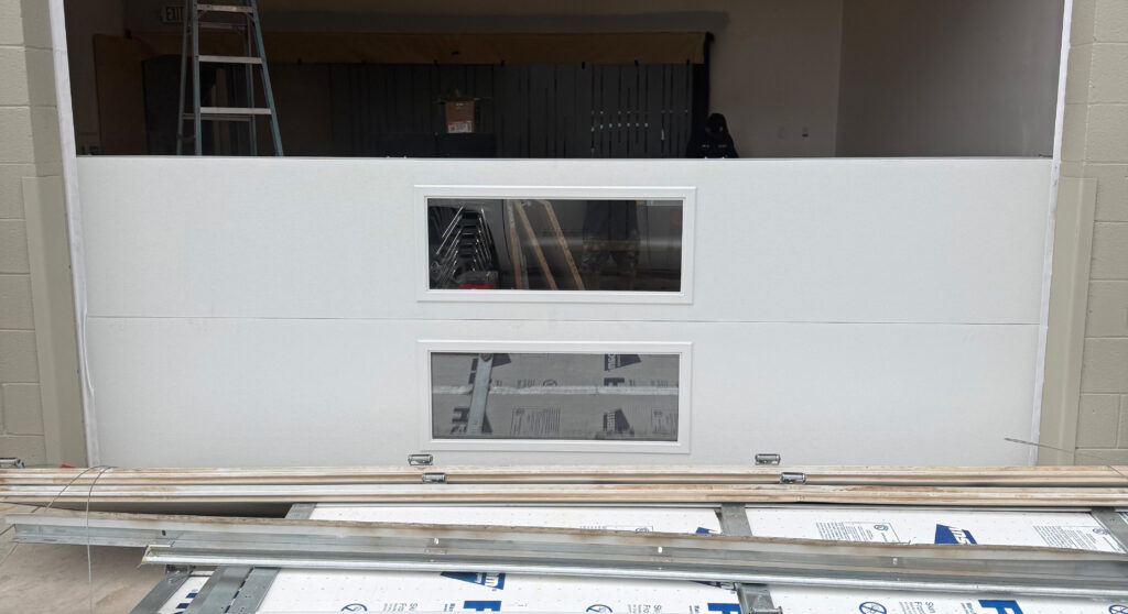 Garage door with windows under installation, showcasing new panels and tools for spring replacement by AZ Garage Door Pros LLC.