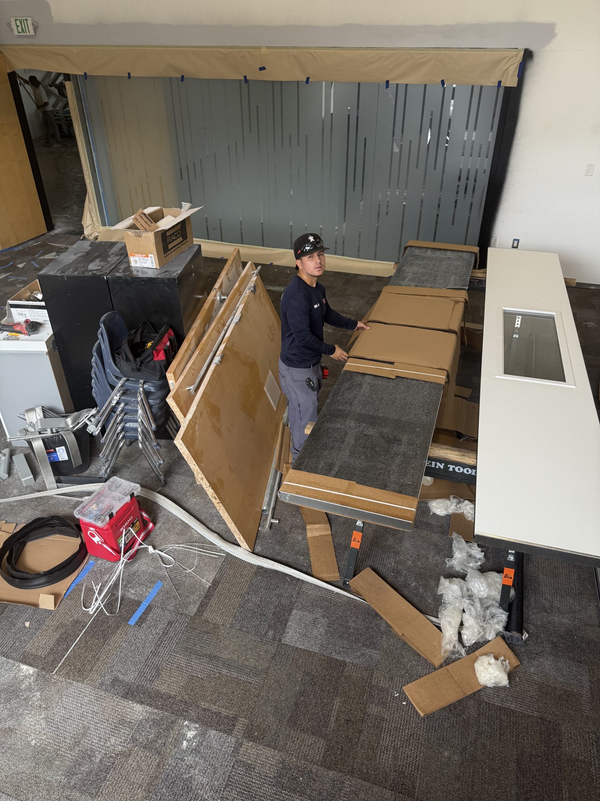 Person assembling and organizing materials in a commercial space, surrounded by tools and furniture, reflecting the hands-on service approach of AZ Garage Door Pros LLC.