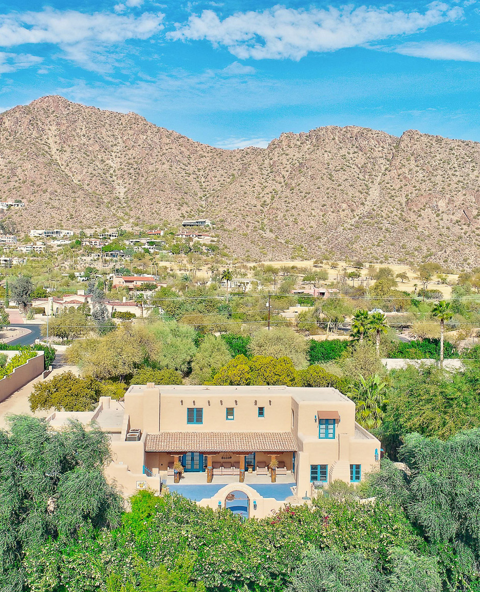 Desert landscape featuring a Southwestern-style home with blue accents, surrounded by greenery and mountains in North Phoenix, Arizona.
