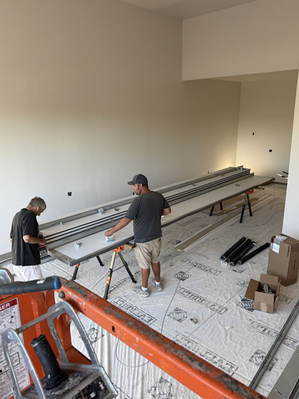 Two technicians assembling garage door components in a spacious indoor setting, with tools and materials visible, emphasizing garage door installation services.